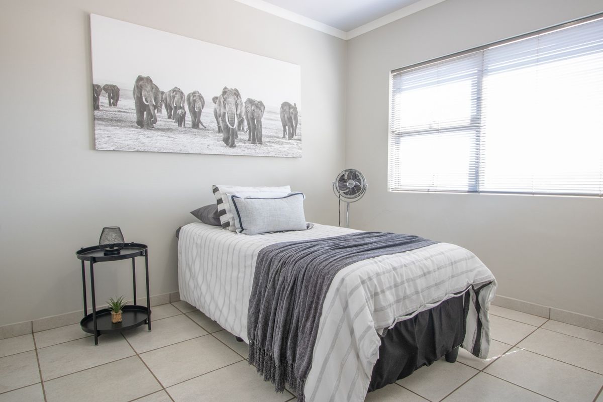 A well-lit bedroom featuring neutral wall tones, tiled flooring, and venetian blinds, providing a clean and functional living space.