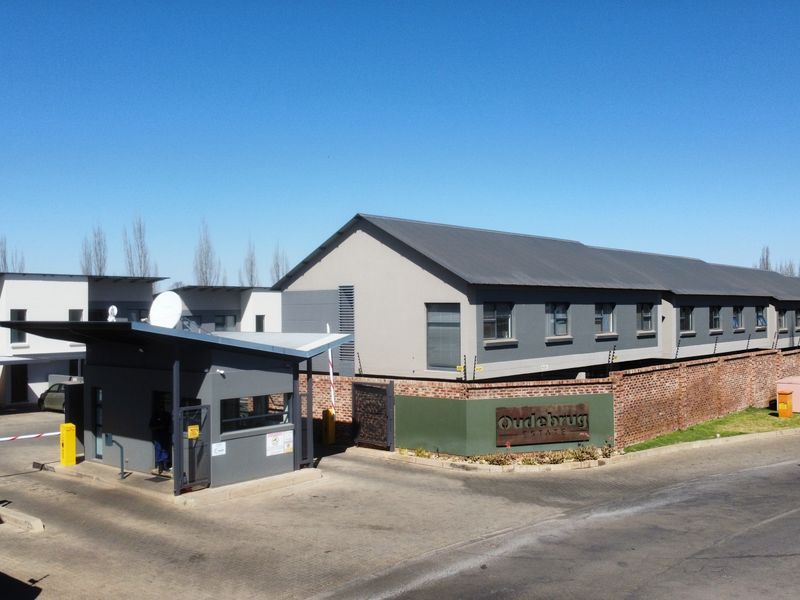 Aerial view of the Oudebrug Estate entrance featuring a modern security gatehouse, brick boundary walls, and electric fencing surrounding the apartment complex.