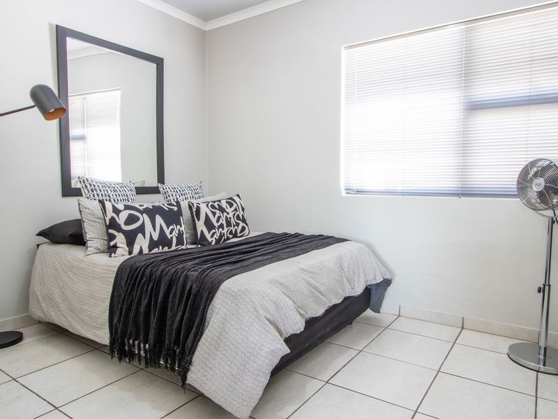 A well-lit bedroom featuring neutral tiled flooring, clean wall finishes, and venetian blinds, providing a simple and functional living space.