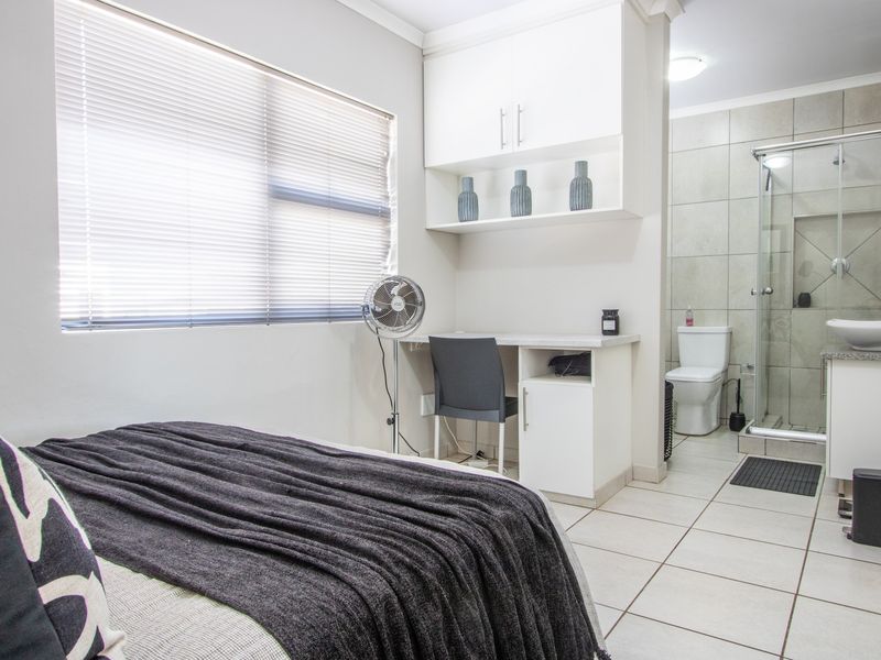A well-maintained bedroom featuring built-in desk and cabinetry, tiled flooring, and an integrated en-suite bathroom with a glass shower enclosure.