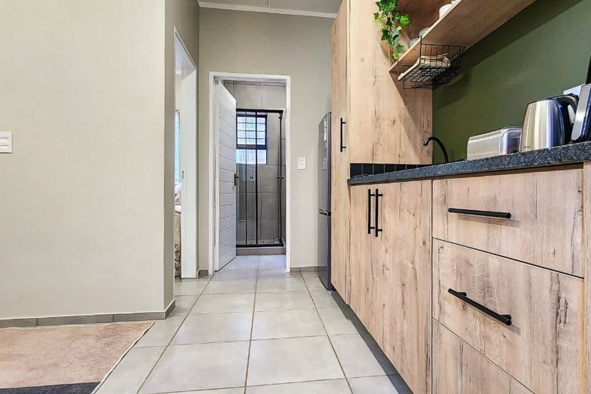 Modern kitchen featuring light wood-look cabinetry, dark stone countertops, and tiled flooring, with a clear view through to the bathroom area.