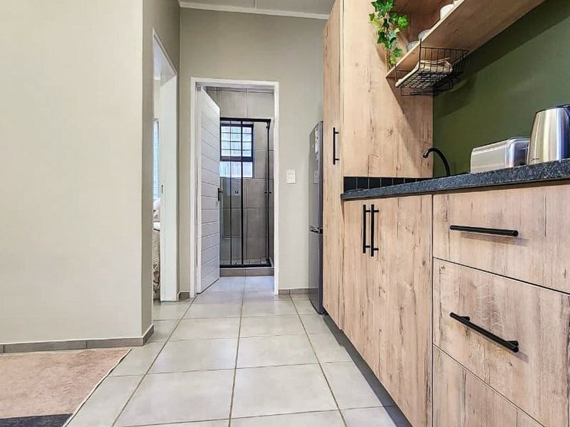 Modern kitchen featuring light wood-look cabinetry, dark stone countertops, and tiled flooring, with a clear view through to the bathroom area.
