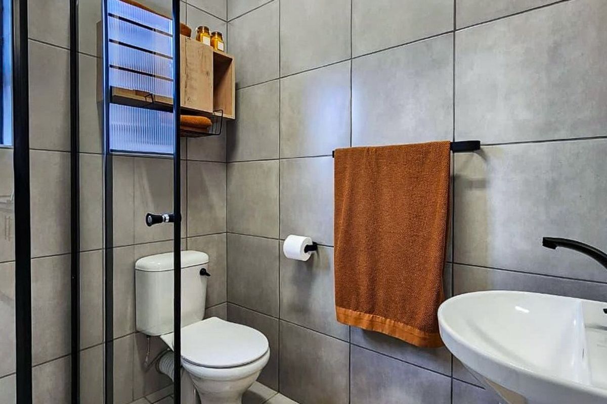 Modern bathroom featuring grey wall tiles, a glass shower enclosure, pedestal basin, and contemporary black fixtures.