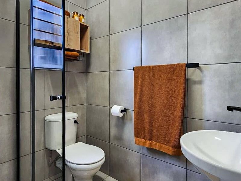 Modern bathroom featuring grey wall tiles, a glass shower enclosure, pedestal basin, and contemporary black fixtures.