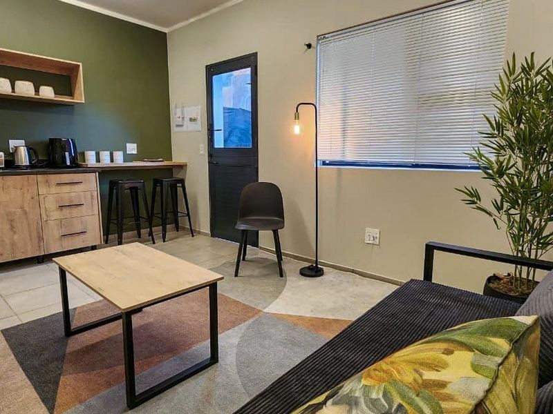 An open-plan living area featuring a compact kitchenette with built-in cabinetry, tiled flooring, and a functional layout with direct access to an external door.