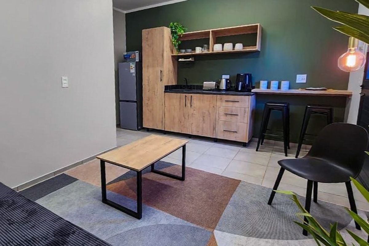 Modern open-plan living area featuring a compact kitchenette with wood-finish cabinetry, open shelving, and a breakfast bar counter.