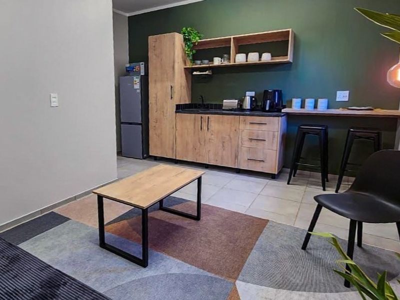 Modern open-plan living area featuring a compact kitchenette with wood-finish cabinetry, open shelving, and a breakfast bar counter.