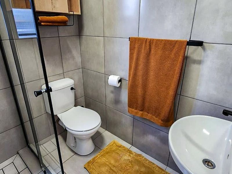 Modern bathroom featuring grey wall tiles, a glass shower enclosure, a white toilet, and contemporary black tapware.