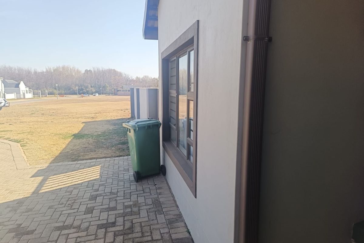 Side exterior view of the property featuring paved walkway, aluminium window frames, and vertical downpipe drainage system.