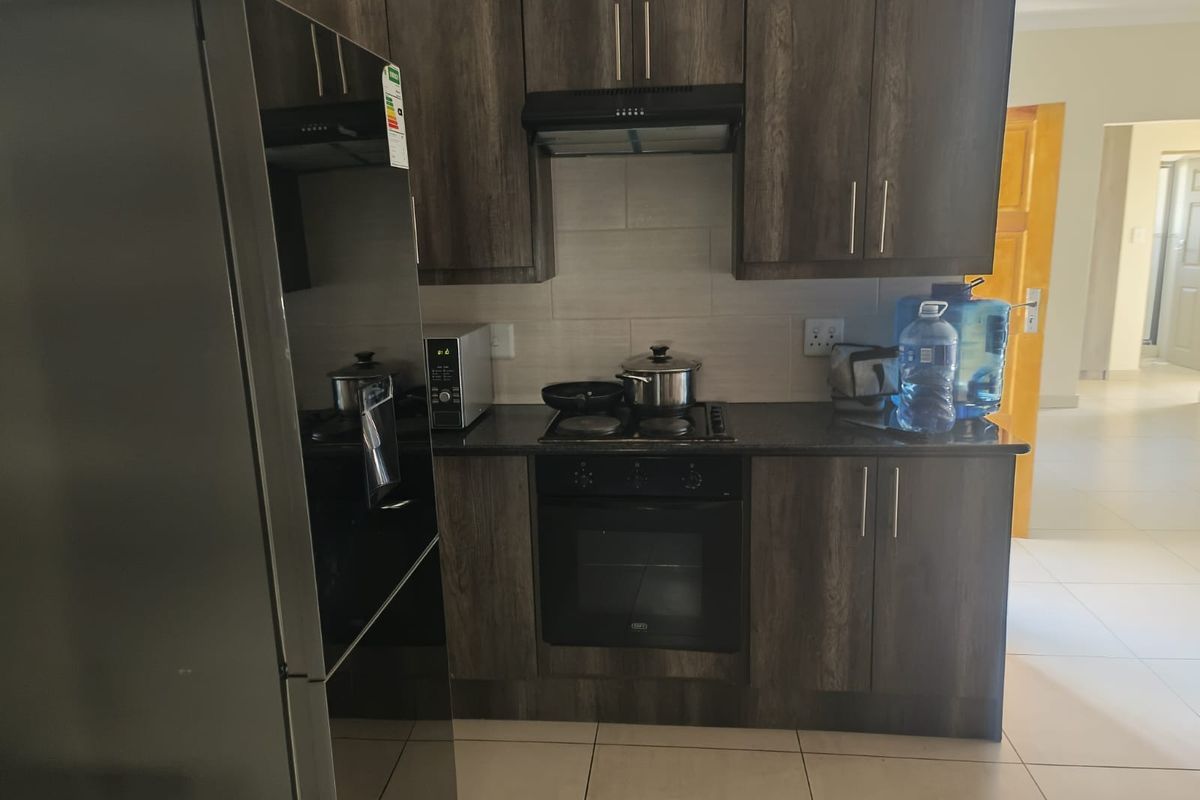 A compact kitchen featuring dark wood-grain cabinetry, granite countertops, a built-in oven, and a hob with an extractor fan.