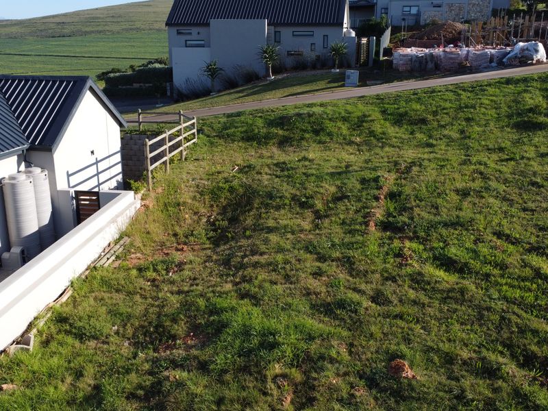 Aerial view of a residential vacant land plot featuring a gentle slope, boundary fencing, and adjacent residential development.