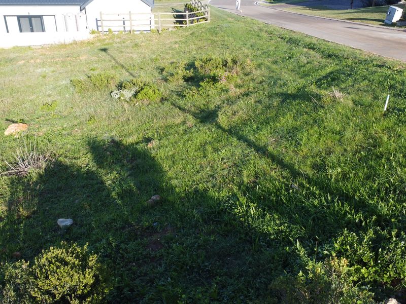 An elevated view of a vacant residential plot featuring a grass lawn and boundary fencing, situated adjacent to a paved road.