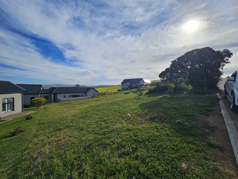 A view of a vacant residential plot featuring a grassy landscape with adjacent homes and a clear view of the surrounding area.