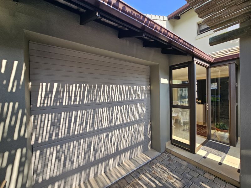 Exterior view of the property featuring a garage door, paved driveway, and a modern glass entrance door with a timber pergola overhead.