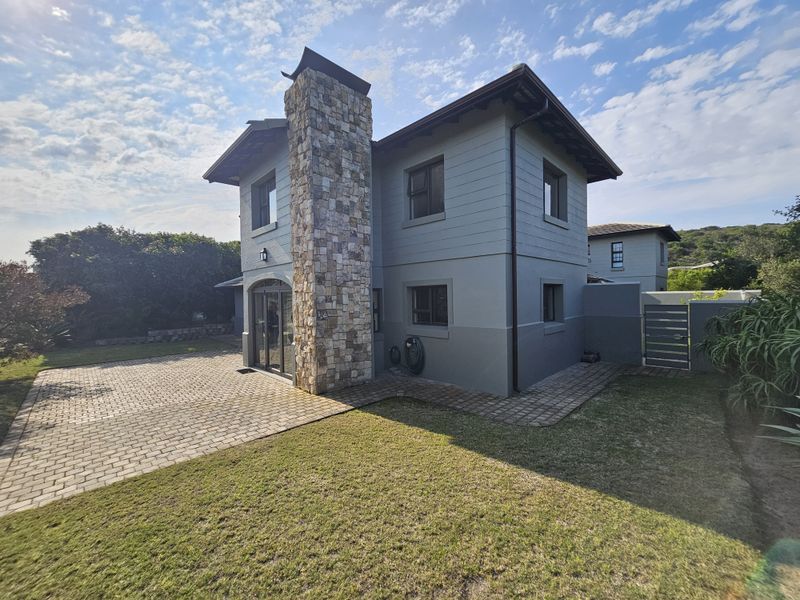 Rear view of the duet property featuring a stone-clad chimney, paved driveway, and well-maintained exterior walls with aluminium window frames.