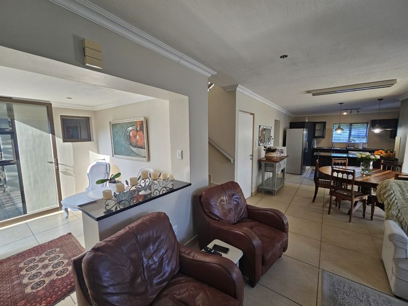 Spacious open-plan living and dining area featuring tiled floors, a granite breakfast counter, and seamless flow to the kitchen and outdoor patio.