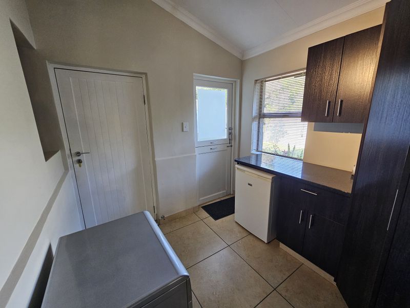 A functional scullery area featuring dark built-in cabinetry, stone-look countertops, tiled flooring, and direct access to the exterior.
