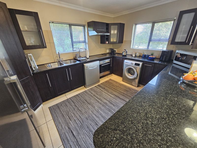 A well-maintained kitchen featuring dark wood cabinetry, granite countertops, a double basin sink, and integrated appliances, offering a functional and modern workspace.