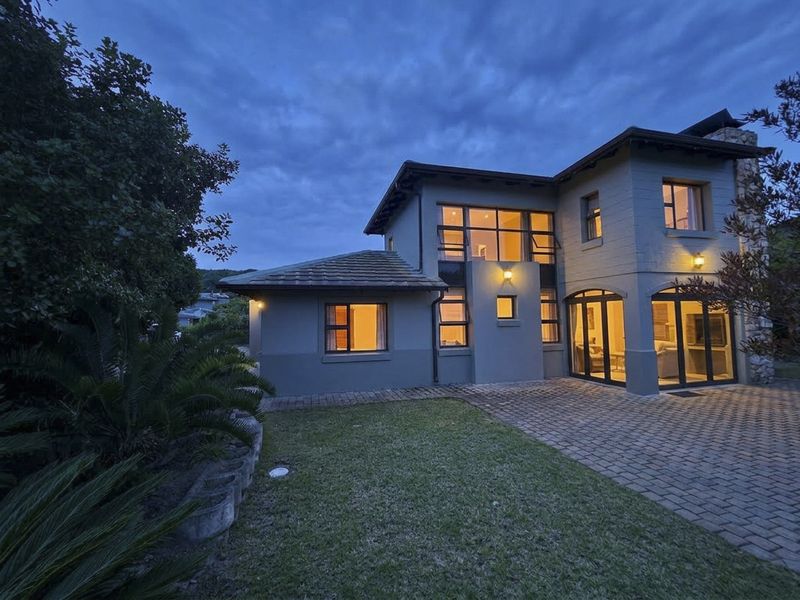 A well-maintained double-storey duet property featuring a paved rear patio, stone cladding accents, and modern aluminium window frames at dusk.
