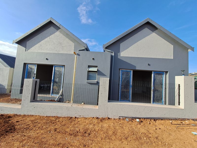 Front view of a modern semi-detached house under construction, featuring dual gables, plastered exterior walls, and secure boundary fencing.