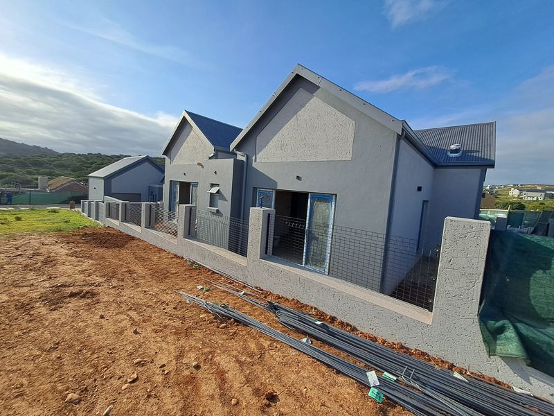 Rear view of a modern residential property under construction, featuring plastered walls, metal roofing, and a perimeter boundary wall with wire mesh fencing.