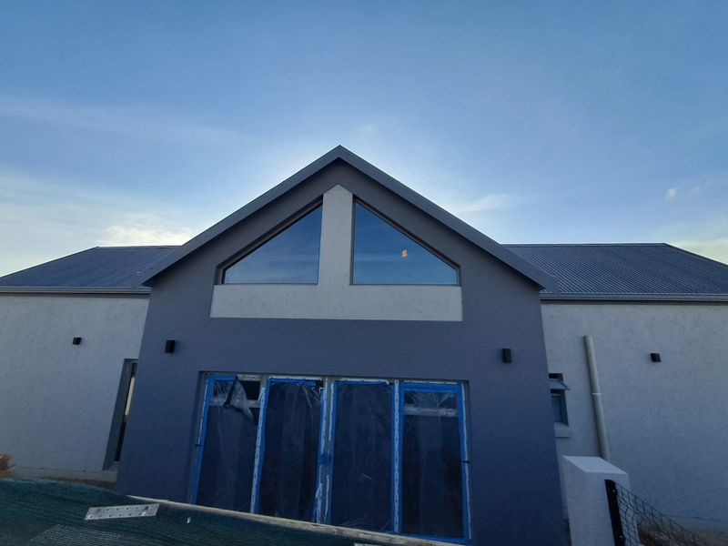 Rear elevation of a modern house featuring a pitched roof, large triangular gable windows, and sliding glass doors with protective construction film still attached.