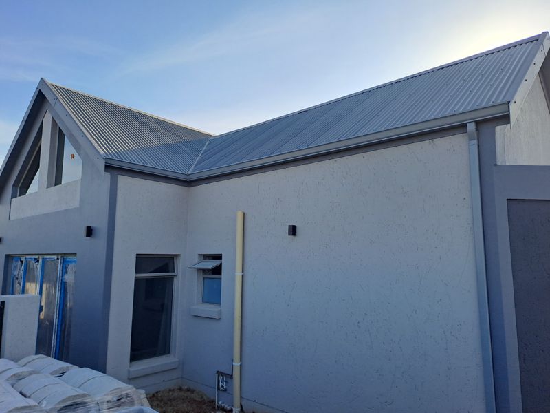 A view of the rear exterior facade featuring modern plastered walls, a corrugated metal roof, and aluminium window frames.