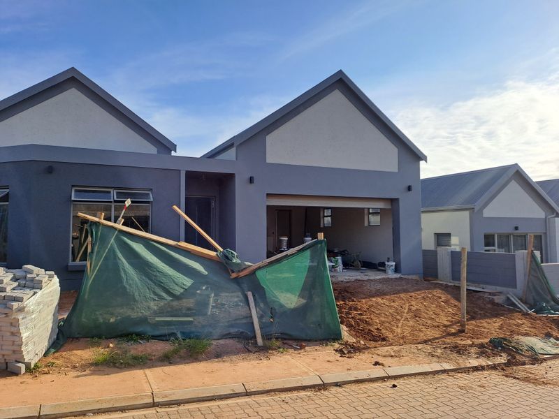 Front elevation of a modern house under construction, featuring a double garage, plastered exterior walls, and ongoing site development.