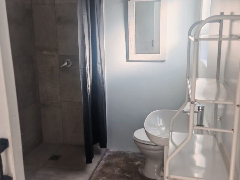 A functional bathroom featuring a tiled shower enclosure, pedestal basin, and toilet, with a neutral color palette.