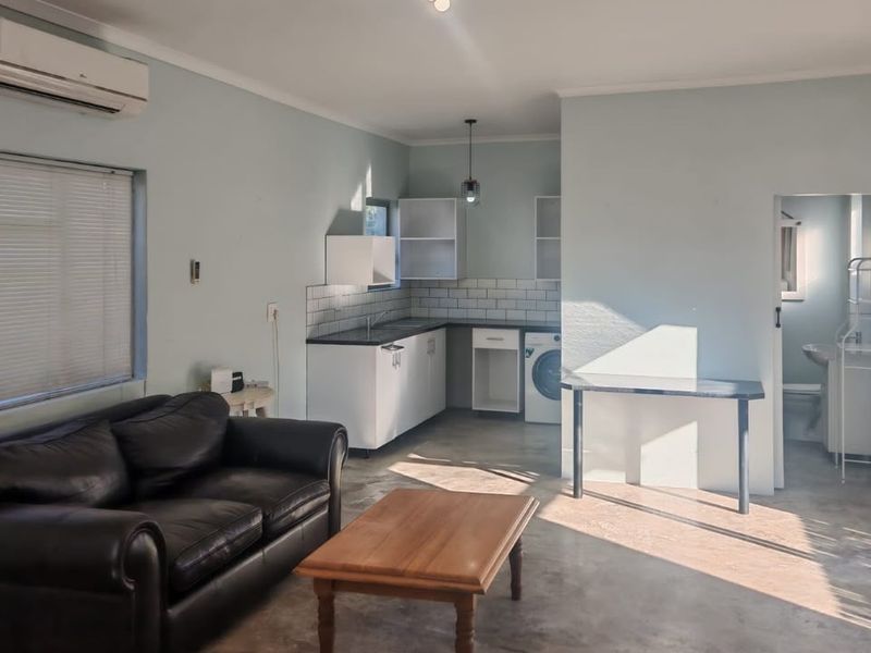 Open-plan living area featuring a compact kitchen with subway tile backsplash, built-in cabinetry, and direct access to an adjacent bathroom.