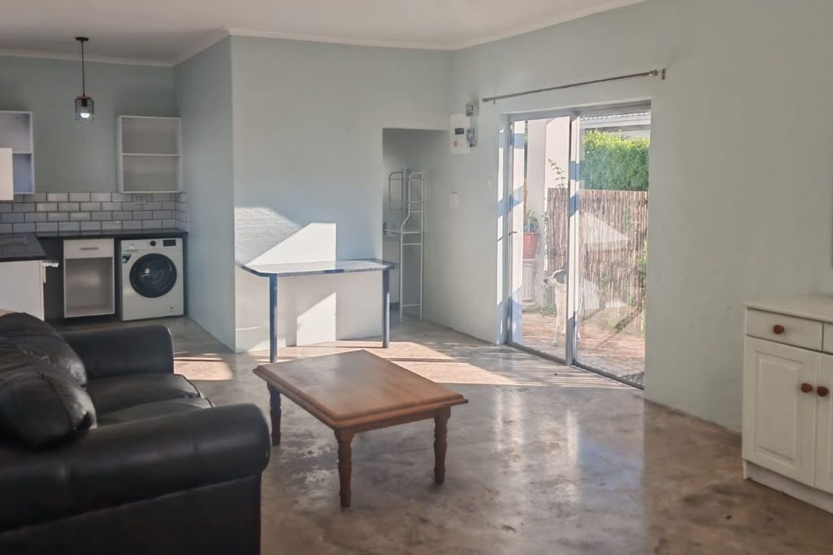 Open-plan living area featuring a compact kitchen with subway tile backsplash, polished concrete floors, and sliding glass doors leading to an outdoor space.