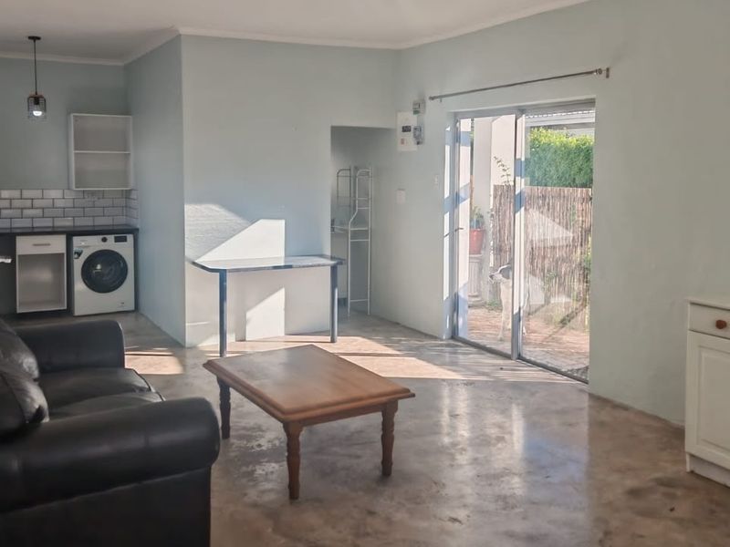 Open-plan living area featuring a compact kitchen with subway tile backsplash, polished concrete floors, and sliding glass doors leading to an outdoor space.
