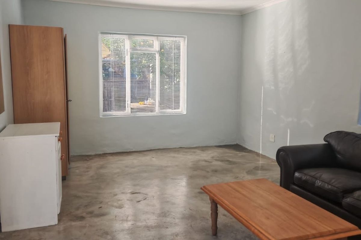 A living room featuring polished concrete floors, aluminium window frames with venetian blinds, and neutral wall finishes.