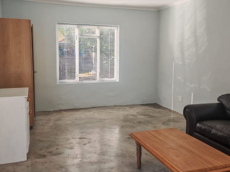 A living room featuring polished concrete floors, aluminium window frames with venetian blinds, and neutral wall finishes.