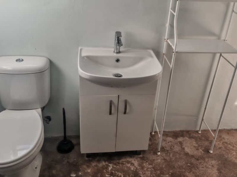 A functional bathroom featuring a white toilet and a vanity basin with a mixer tap, currently requiring flooring completion.