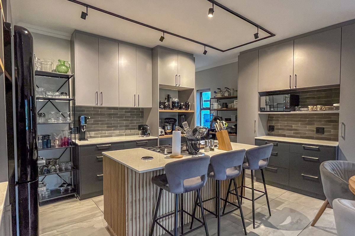 Modern kitchen featuring two-tone cabinetry, a central island with stone countertops, subway tile backsplash, and contemporary track lighting.