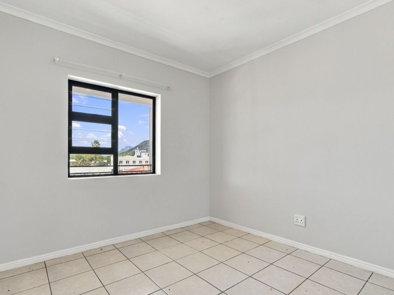 A bright, empty bedroom featuring neutral wall paint, tiled flooring, and an aluminium-framed window with views.