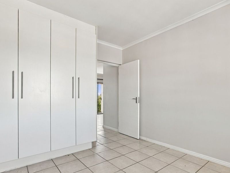 A bright, empty bedroom featuring neutral tiled flooring and ample built-in cupboard storage space.