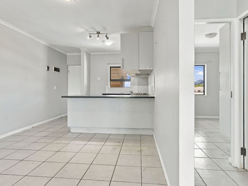 An open-plan living and kitchen area featuring tiled flooring, neutral walls, and a functional breakfast bar layout, presented in a vacant state.