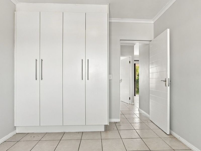A bright, empty bedroom featuring built-in wardrobes, tiled flooring, and neutral wall finishes, providing a clean canvas for personalization.