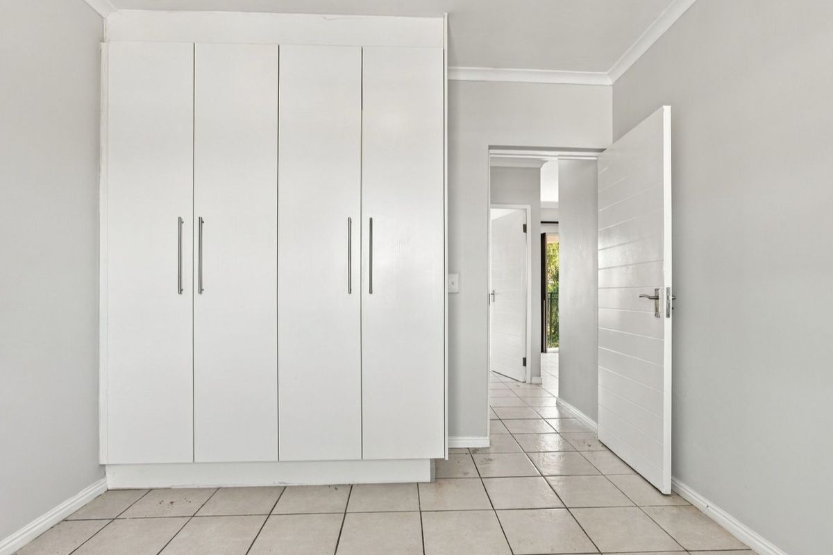 A bright, empty bedroom featuring built-in wardrobes, tiled flooring, and neutral wall finishes, providing a clean canvas for personalization.