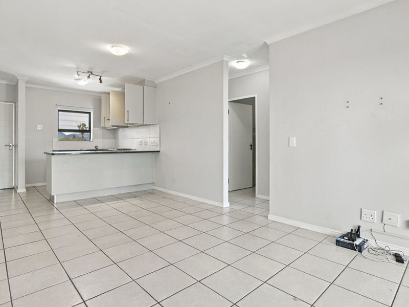 An open-plan living and kitchen area featuring neutral tiled flooring, built-in cabinetry, and a functional kitchen layout in a well-maintained apartment.