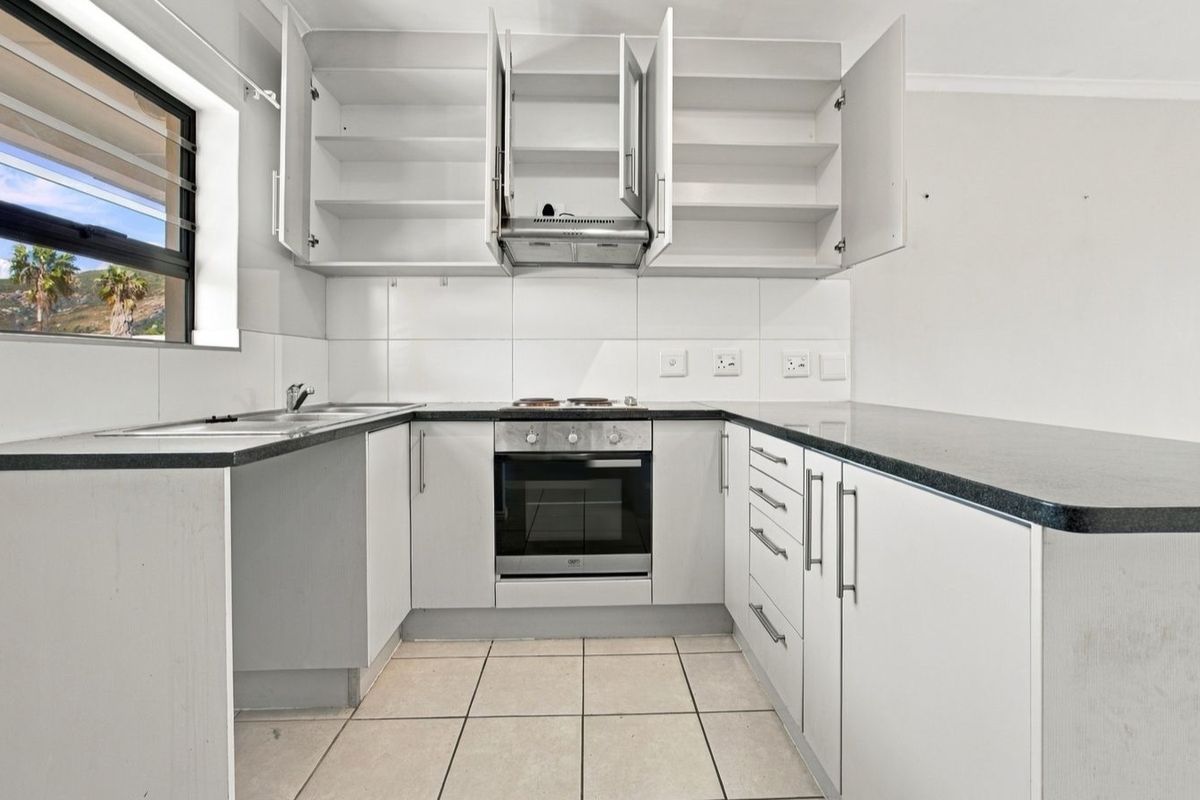 A functional kitchen featuring white cabinetry, dark laminate countertops, built-in oven, hob, extractor fan, and tiled flooring.