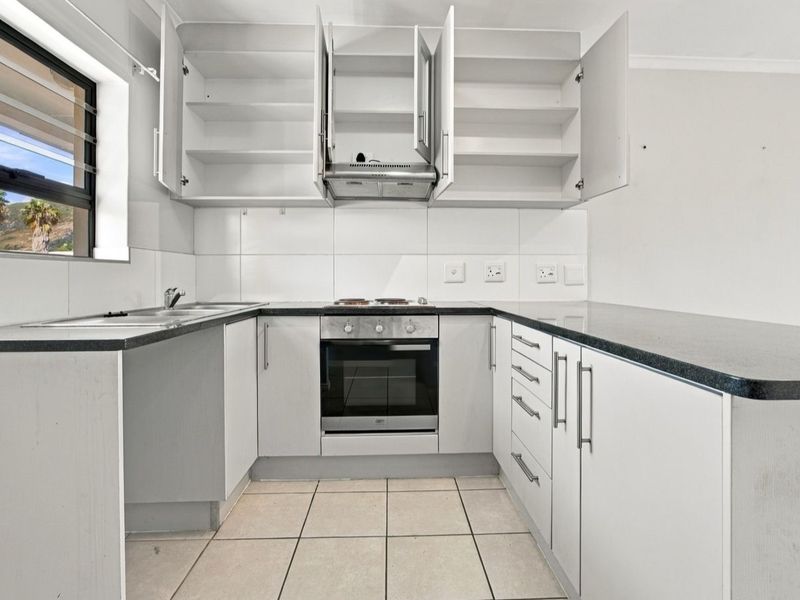 A functional kitchen featuring white cabinetry, dark laminate countertops, built-in oven, hob, extractor fan, and tiled flooring.