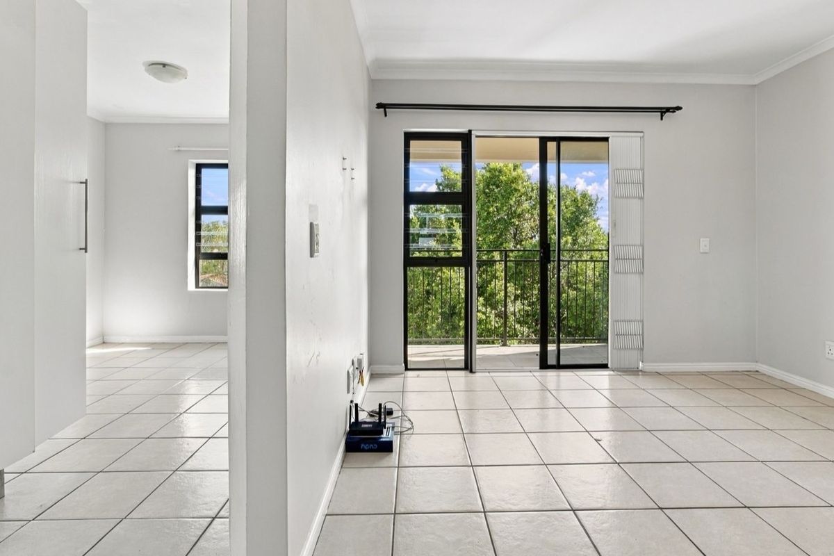 Bright and spacious living area featuring neutral ceramic floor tiles, clean white walls, and direct access to a private balcony through sliding glass doors.