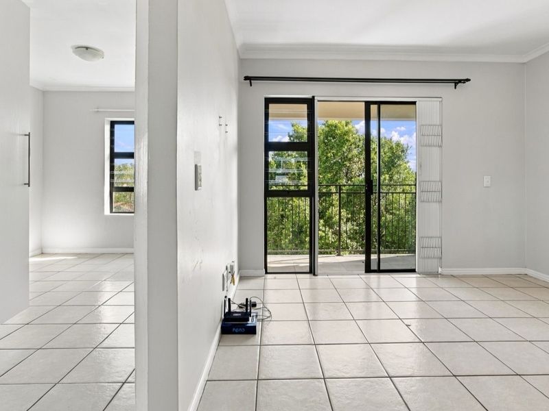 Bright and spacious living area featuring neutral ceramic floor tiles, clean white walls, and direct access to a private balcony through sliding glass doors.