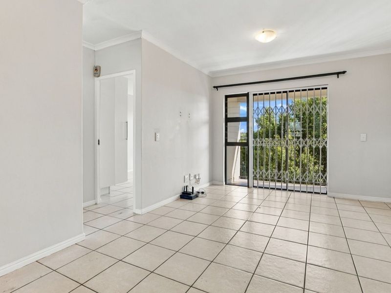 An empty, tiled living room featuring a sliding glass door with a security gate, providing access to an outdoor area.