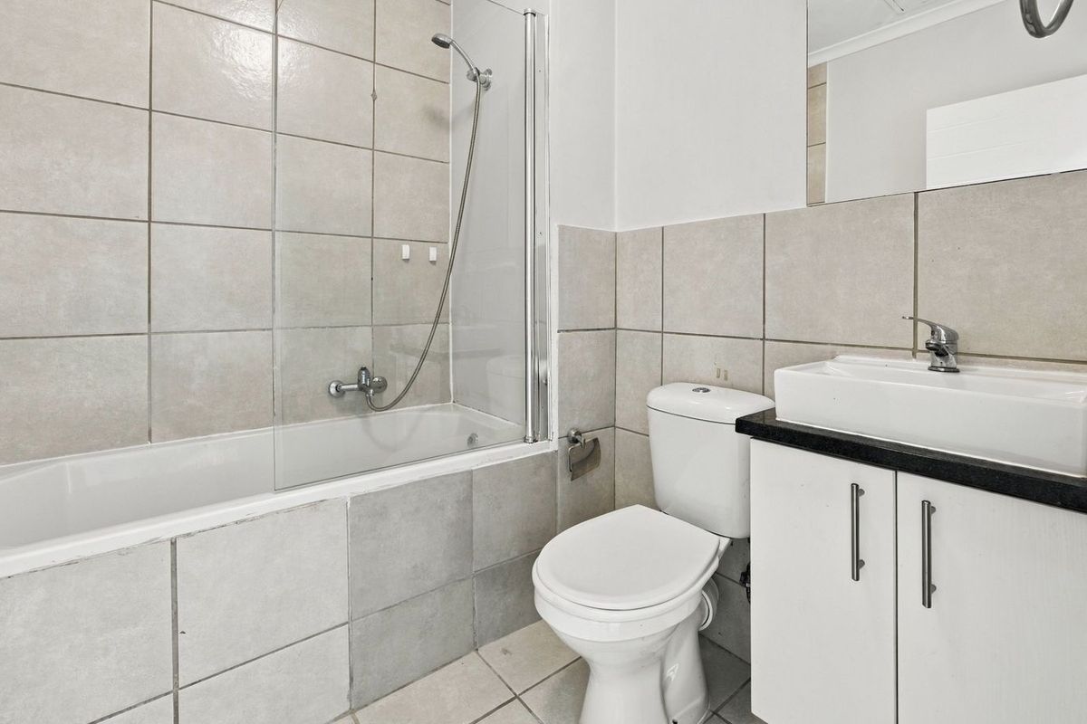 A functional bathroom featuring a bathtub with a glass screen, a vanity with a countertop basin, and neutral wall tiling.