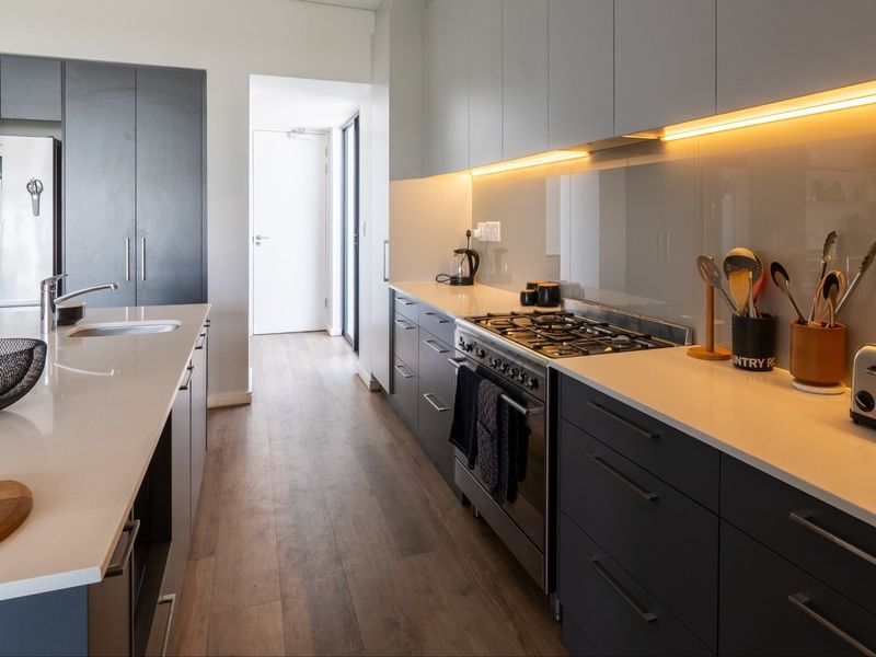 Modern kitchen featuring sleek dark cabinetry, stone countertops, a central island, and high-quality integrated appliances with warm under-cabinet lighting.
