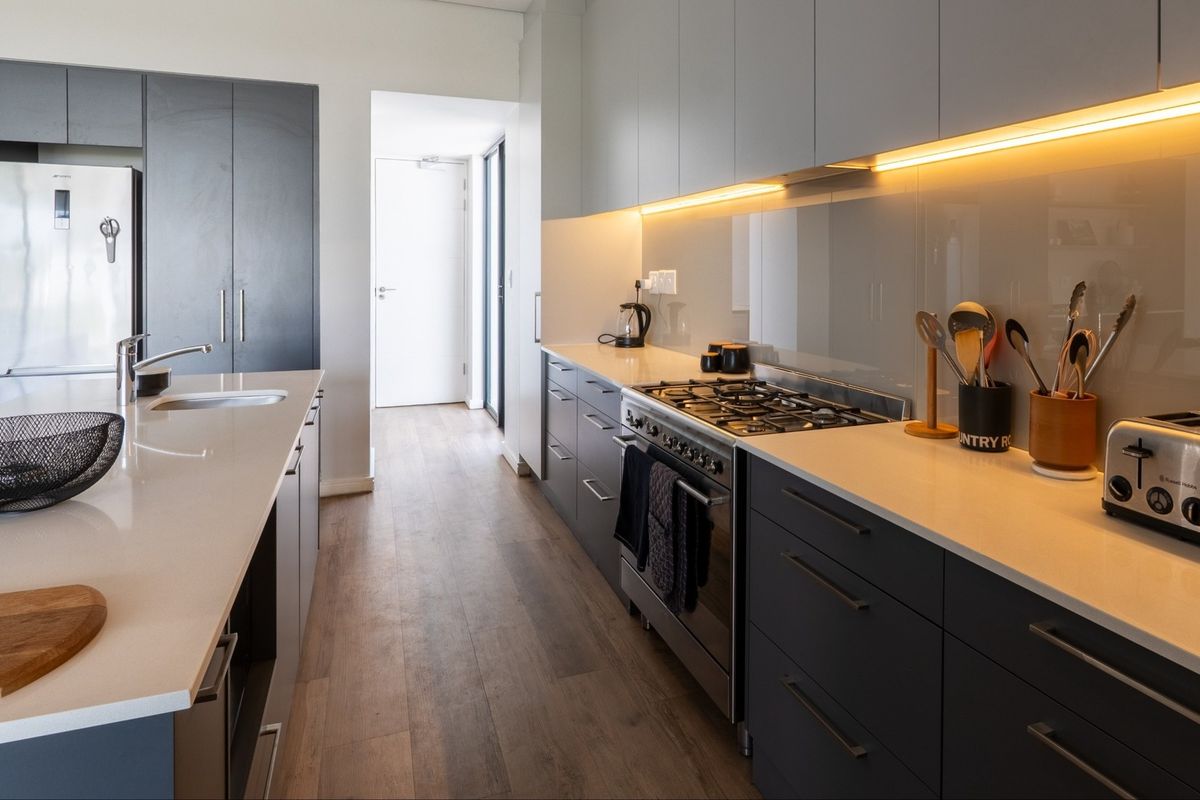 Modern kitchen featuring sleek dark cabinetry, stone countertops, a central island, and high-quality integrated appliances with warm under-cabinet lighting.